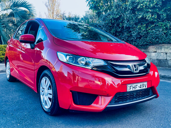 used Honda Jazz for sale - Automatic red 2015 model with low kms and service books - photo showing the front driver side shot from a low angle showing the colour matching front bumper and grille 